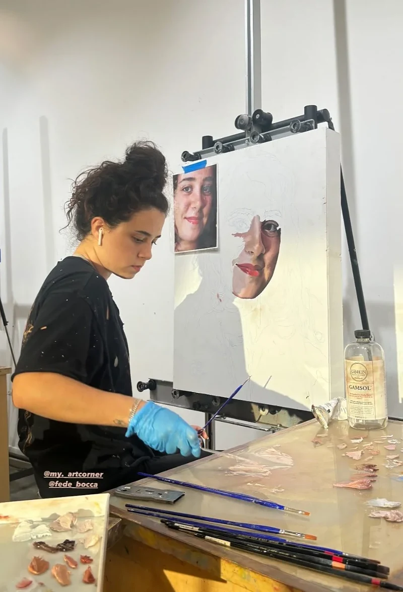 Federica painting a portrait at her easel, wearing blue gloves.
